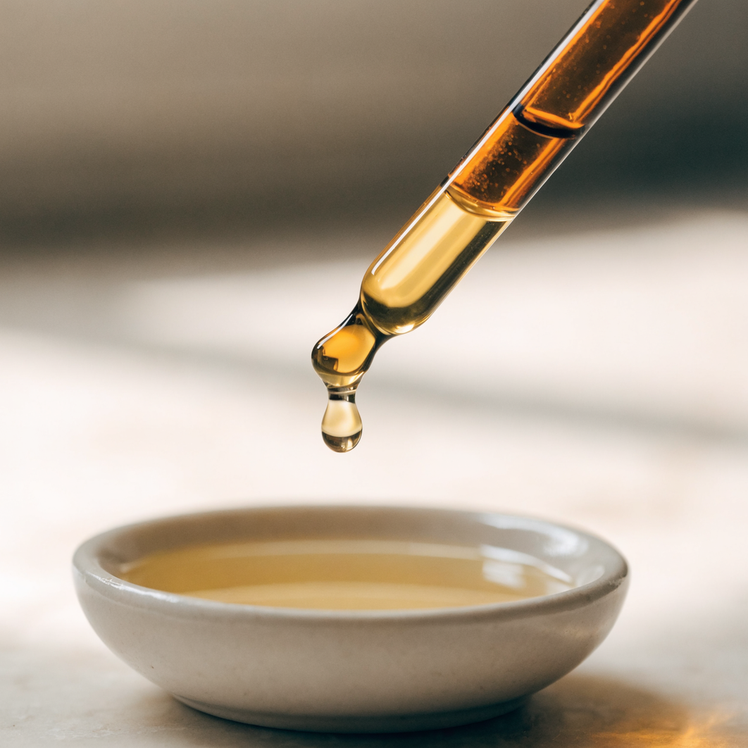 Amber dropper bottle of essential oil being measured into a dish of carrier oil for dilution